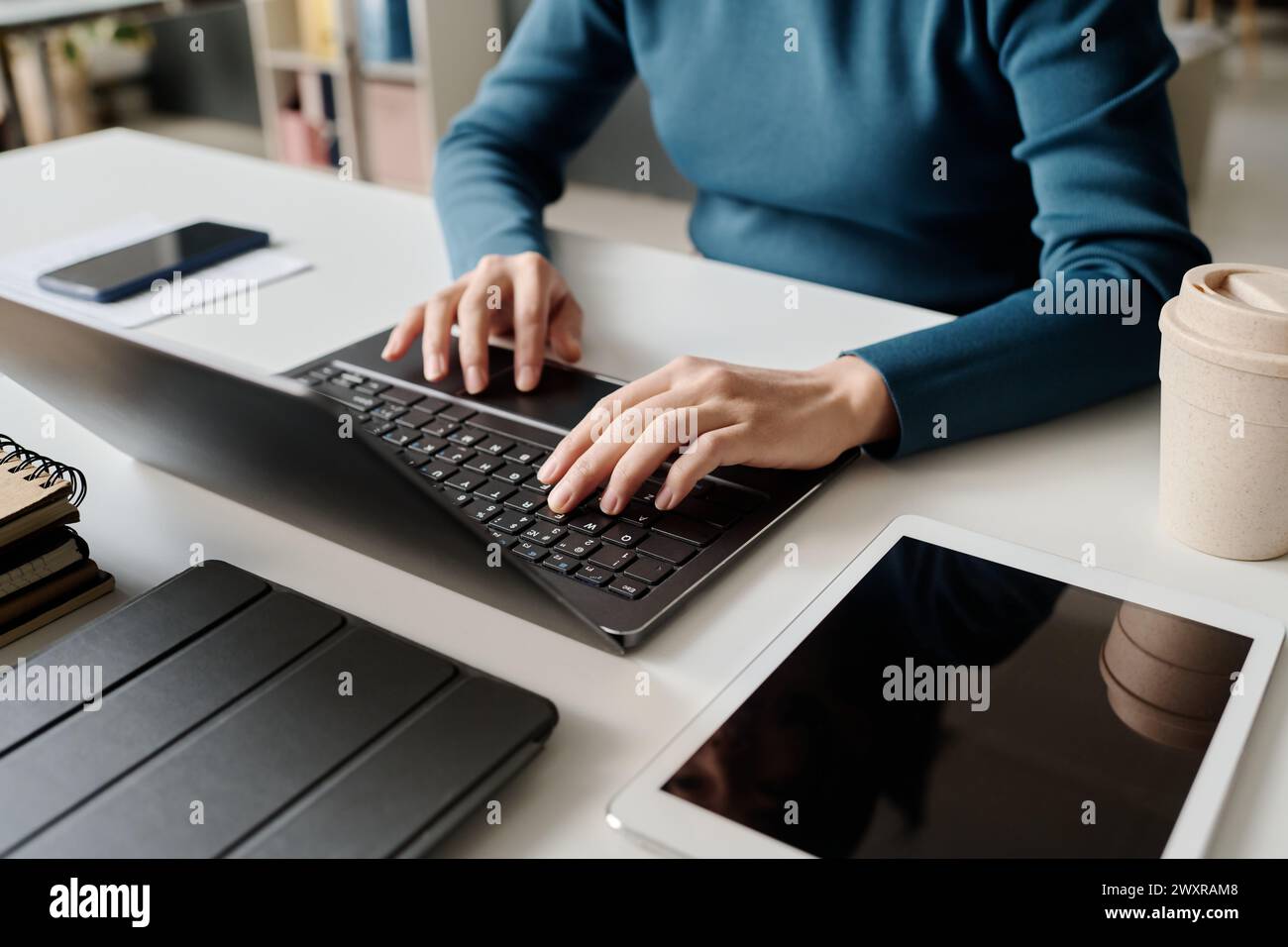 Angle élevé des mains de la femme méconnaissable assise au bureau tapant sur ordinateur portable au lieu de travail dans le bureau moderne Banque D'Images