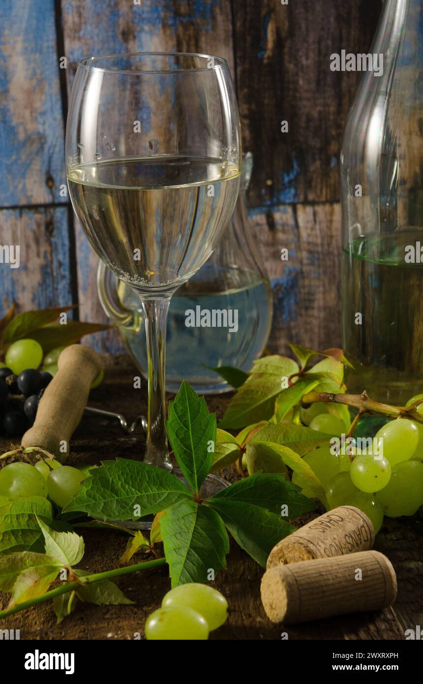 Verre de vin blanc sur un fond en bois avec des raisins, des feuilles et des bouchons de vin. Banque D'Images