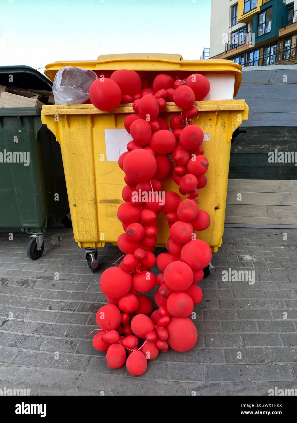 Guirlandes de ballons rouges dans une benne à ordures, foyer sélectif. Décorations usagées jetées. Concept de la mélancolie après la fête de vacances Banque D'Images