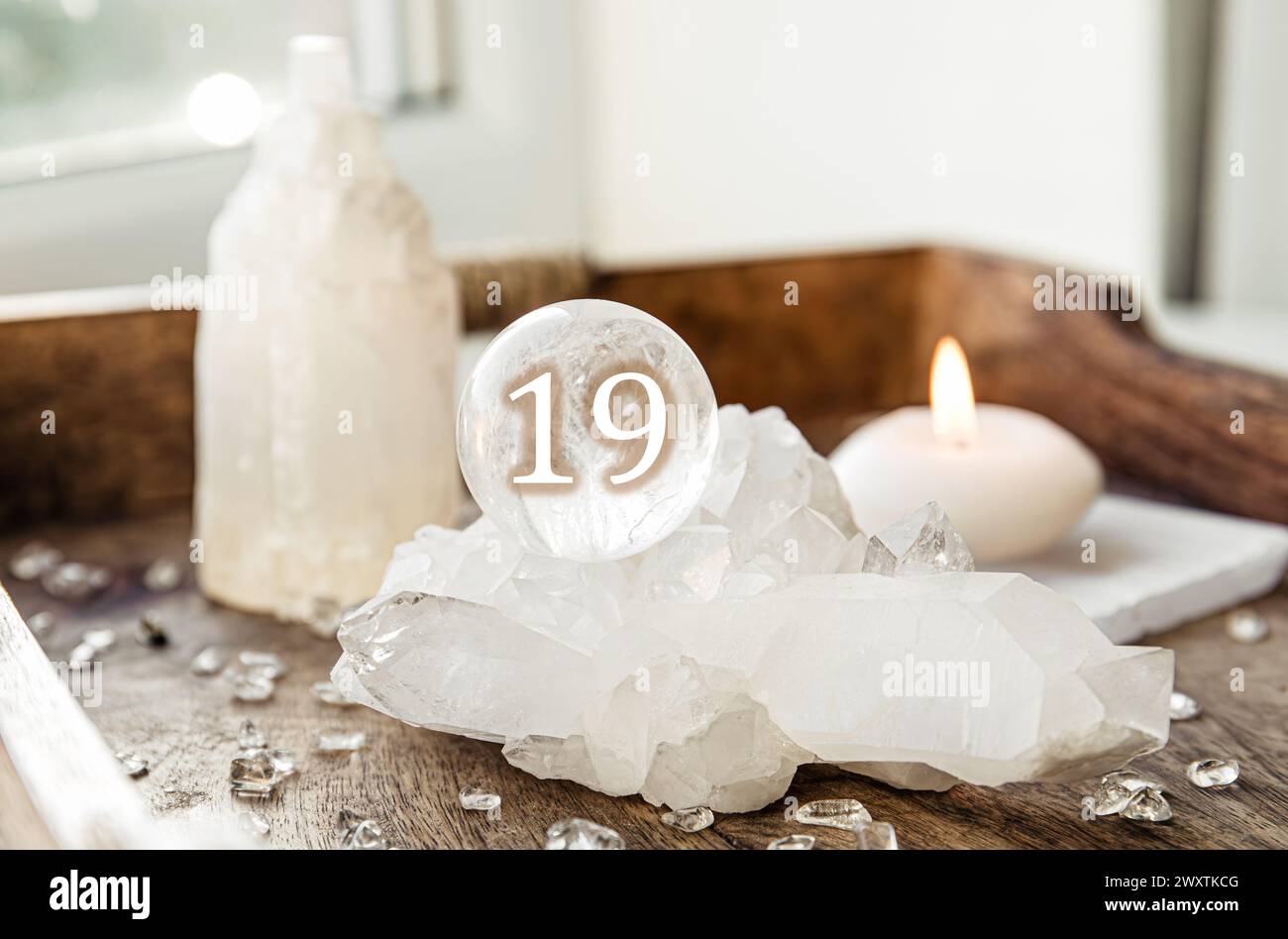 Numéro dix-neuf sur une sphère de pierres précieuses ou boule de cristal connue sous le nom de cristallum orbis ou orbuculum. Boule de quartz clair naturel sur support sur plateau en bois à la maison. Banque D'Images