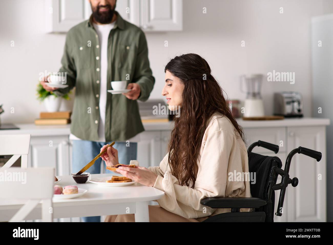 belle femme joyeuse avec un handicap en fauteuil roulant profitant du petit déjeuner avec son mari barbu Banque D'Images