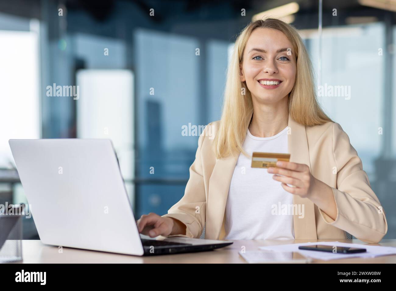 Femme d'affaires confiante utilisant un ordinateur portable et une carte de crédit pour les achats en ligne dans un cadre de bureau moderne. Banque D'Images