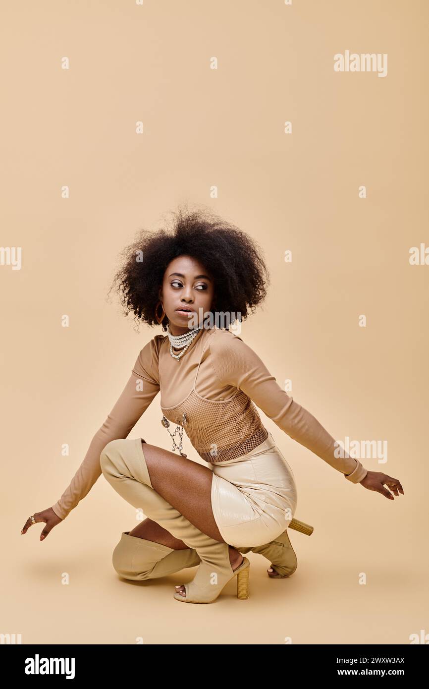 jeune modèle afro-américain dans une tenue pastel élégante et des bottes hautes cuisses assis sur un beige Banque D'Images