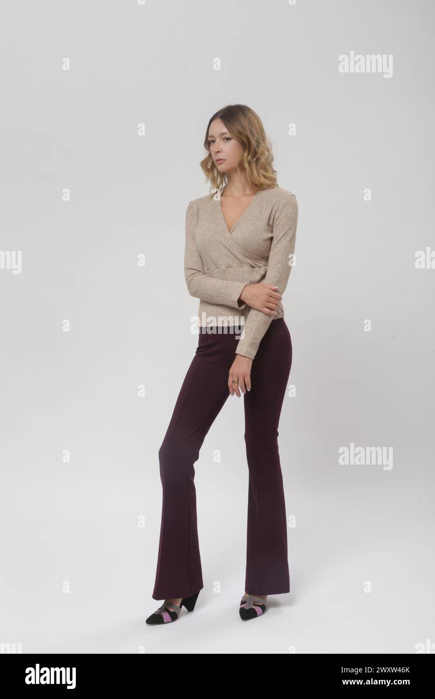 Série de photos de studio de jeune modèle féminin portant un pantalon violet évasé de base et une chemise beige tricotée, collection de mode automne hiver Banque D'Images