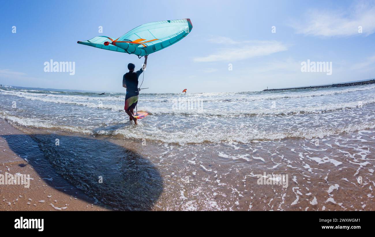 Surfeur athlète surfeur avec voile et planche à voile vers l'océan, photo de l'arrière derrière peu profond vers l'horizon de la mer Banque D'Images