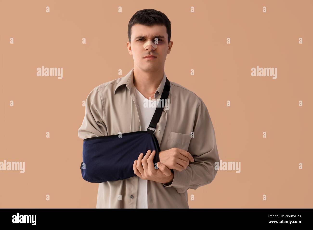 Jeune homme blessé après un accident avec bras cassé sur fond beige Banque D'Images