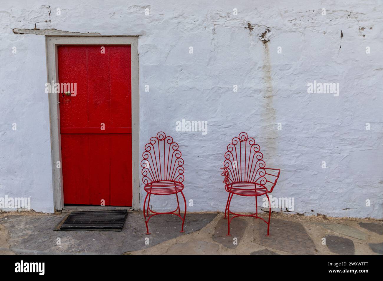 Mur blanc avec une porte rouge vif sur la gauche et deux chaises encadrées en métal peint en rouge devant le mur. Copier l'espace en haut à droite. Banque D'Images