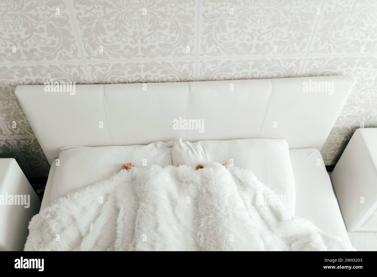 Deux jeunes filles sont allongées sur un lit avec des draps blancs, recouvertes d'une couverture. Banque D'Images
