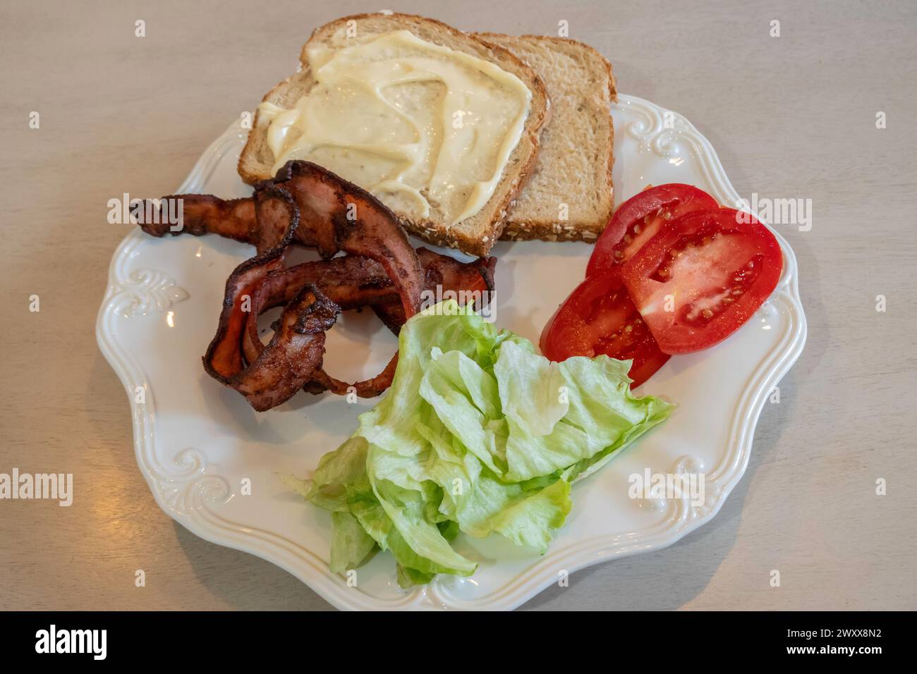 Séparez les ingrédients d'un sandwich bacon, laitue et tomate sur une assiette blanche avec du pain et de la mayonnaise. Banque D'Images