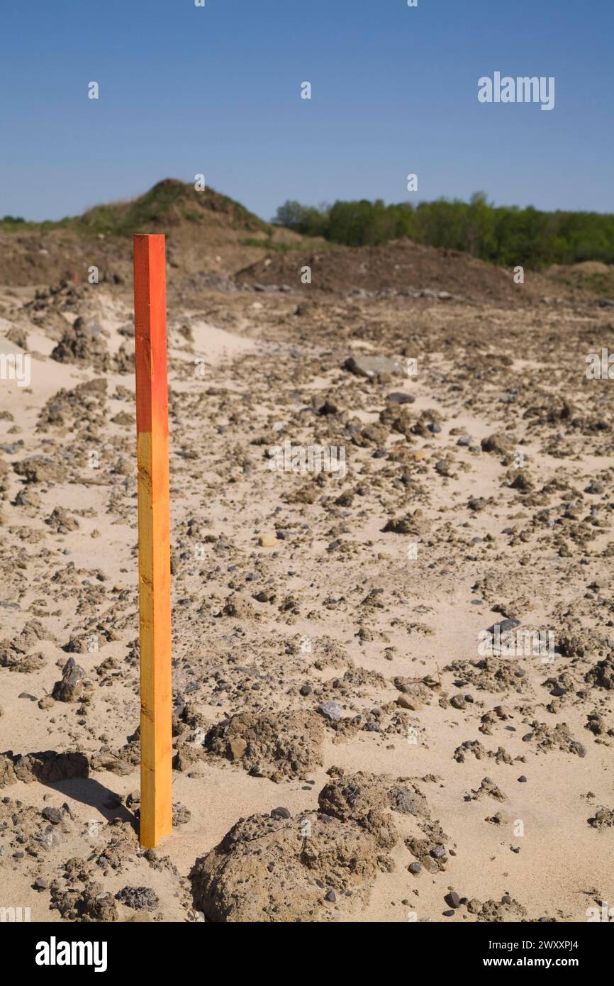 Piquet d'arpenteur en bois peint en rouge et orange ou marqueur dans un sol sablonneux indiquant une ligne de démarcation sur un chantier de construction au printemps, Québec, Canada Banque D'Images