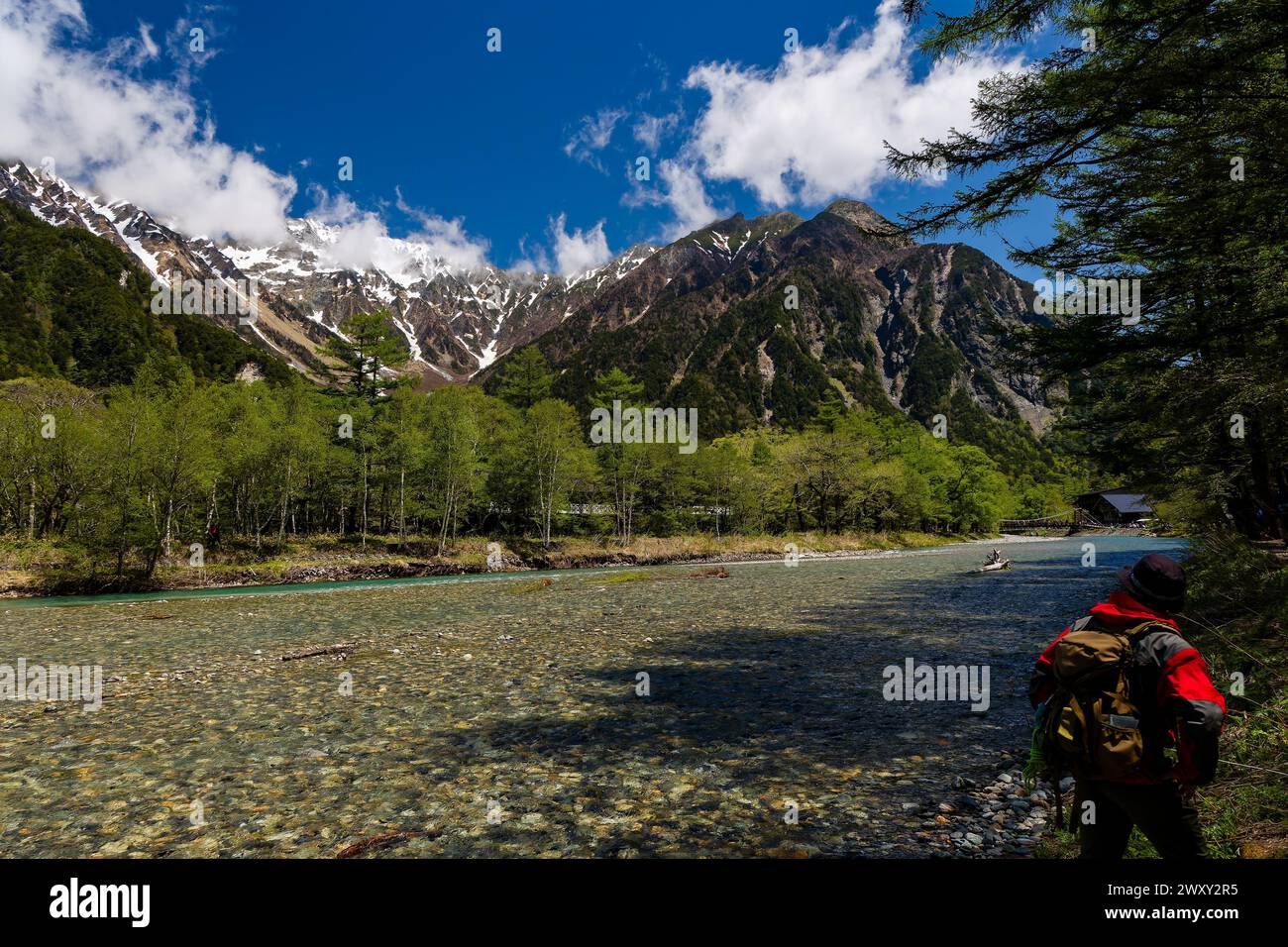 Randonneur à côté d'une rivière claire et rapide en face de sommets enneigés Banque D'Images