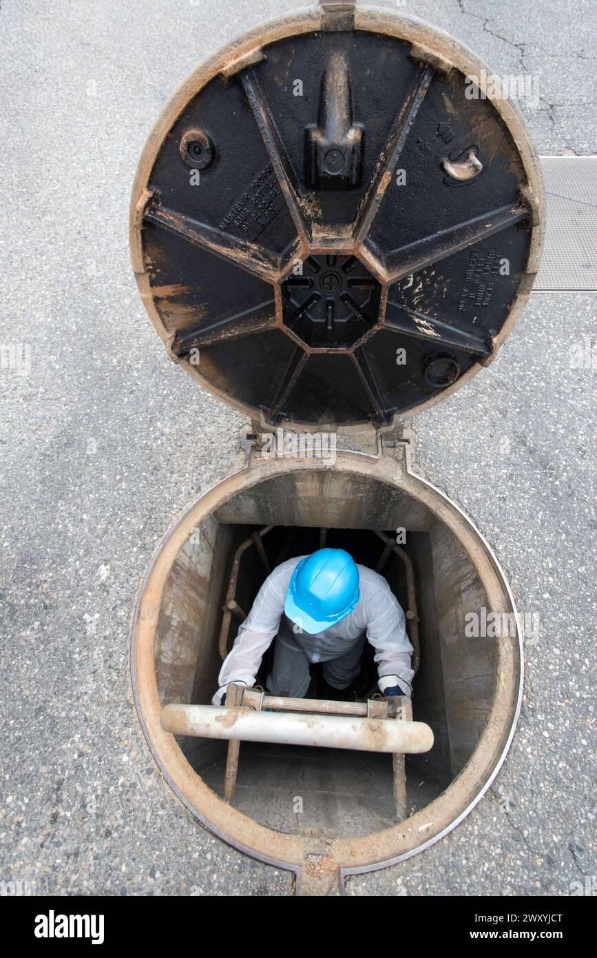 Opération de nettoyage : inspection, nettoyage et rinçage des tuyaux d'égout. Travailleur des eaux usées au travail portant une combinaison blanche et un casque de sécurité. Banque D'Images
