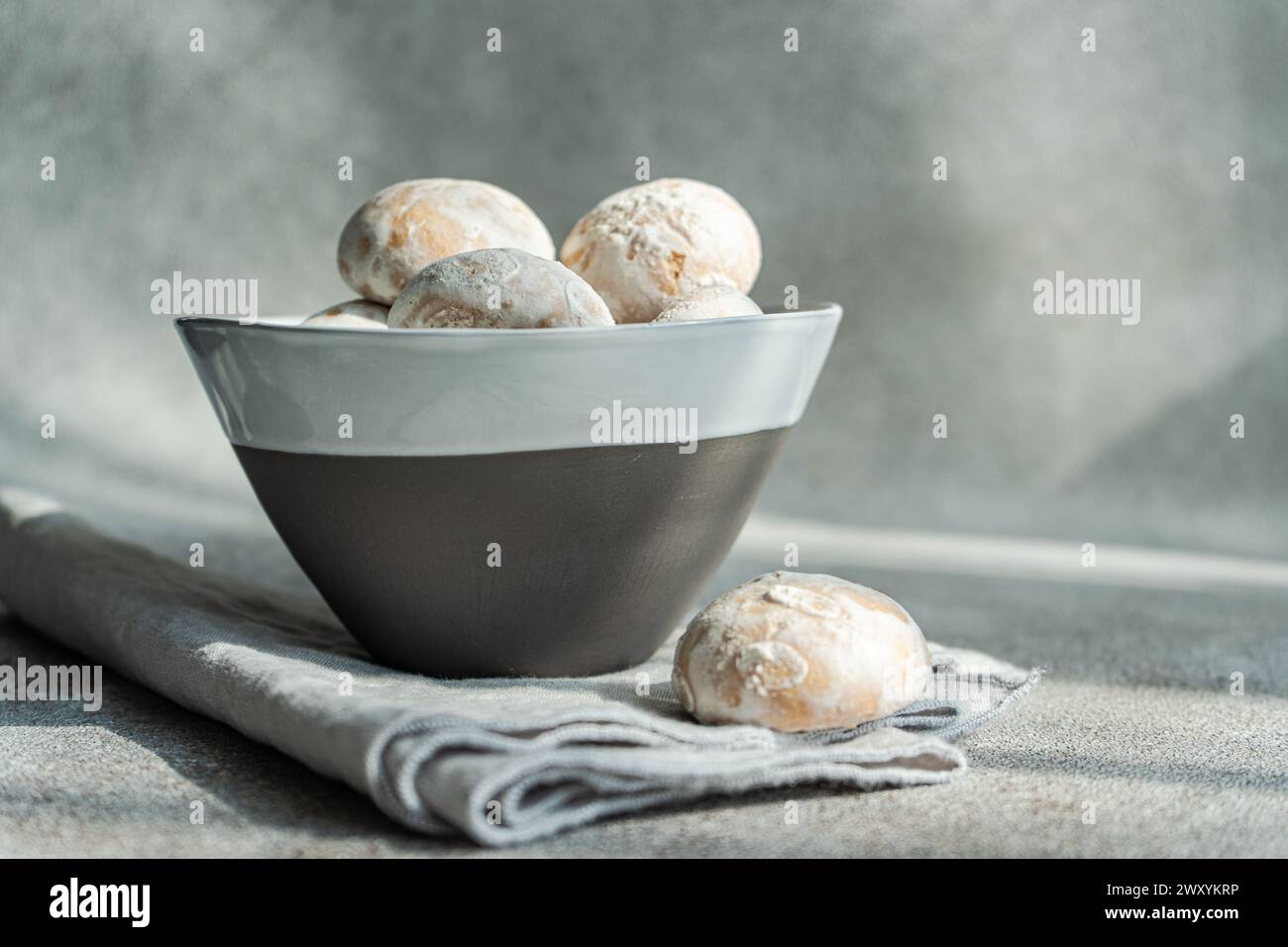 Un bol gris moderne rempli de biscuits enrobés de sucre en poudre sur un lin texturé, avec un éclairage doux améliorant l'atmosphère chaleureuse Banque D'Images