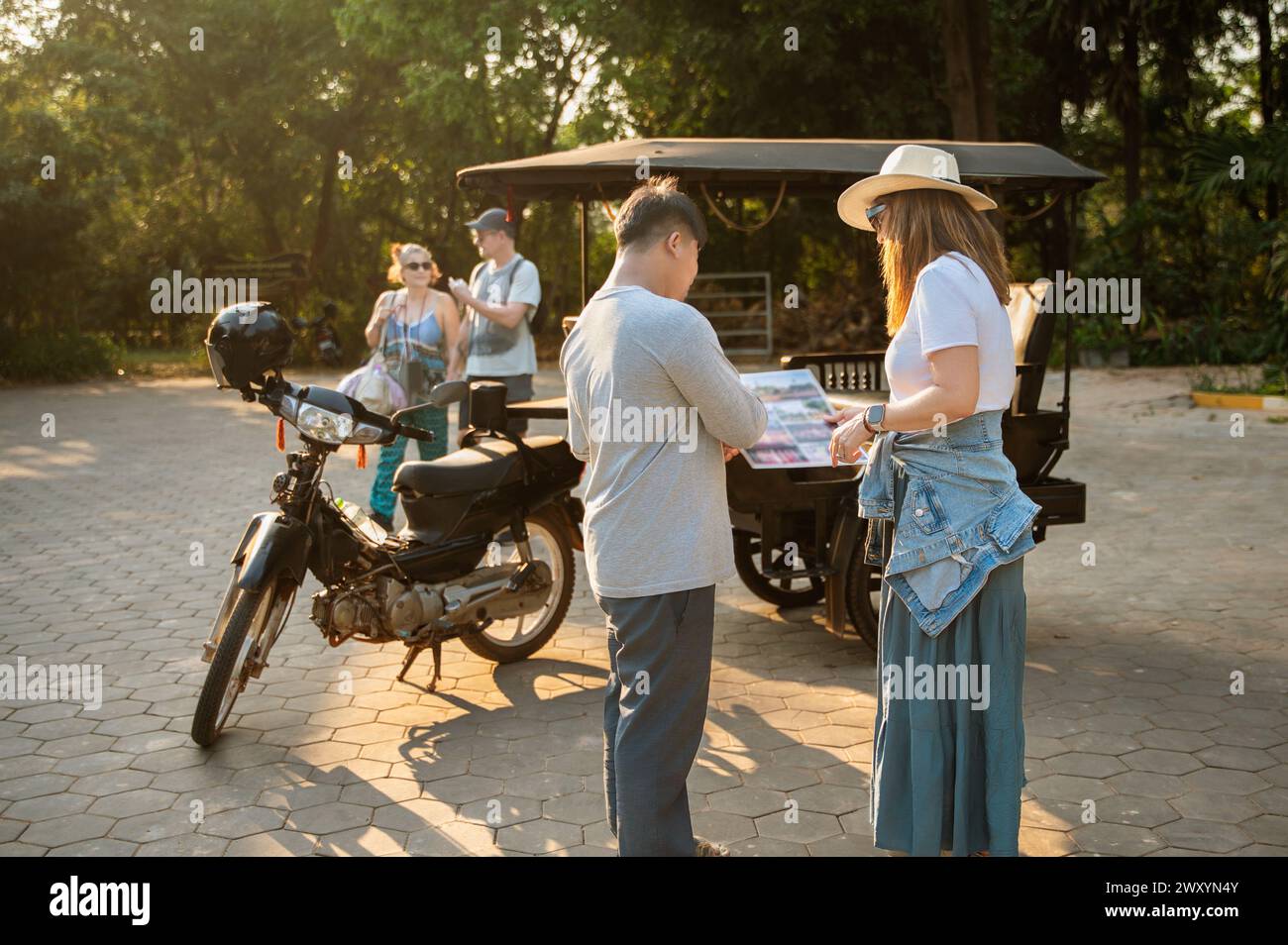 Un couple vérifiant une carte locale à côté d'une moto comme d'autres touristes marchent en arrière-plan Banque D'Images