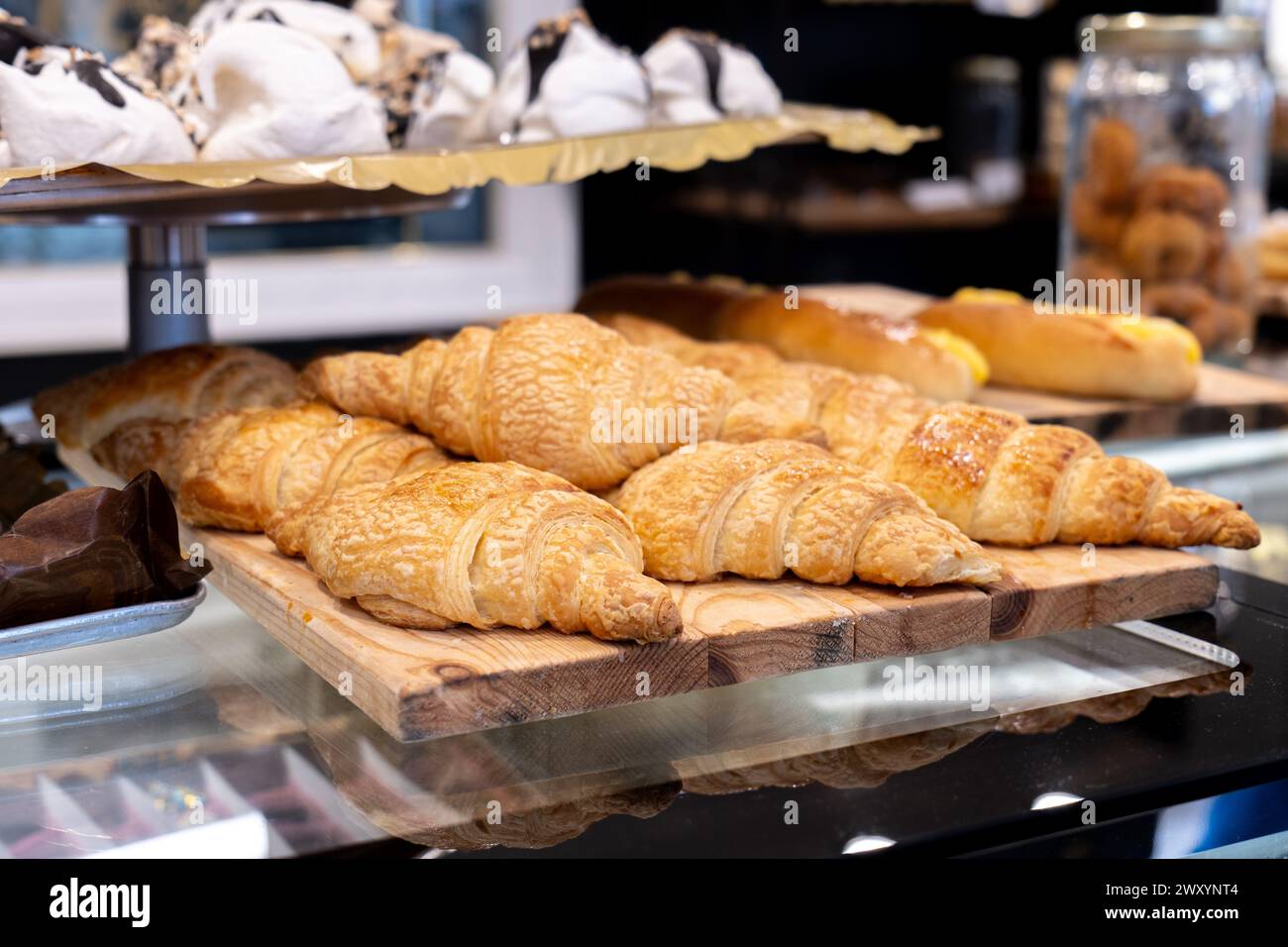 Des croissants dorés fraîchement cuits décorés avec goût sur une planche de bois rustique dans une vitrine en verre de boulangerie Banque D'Images