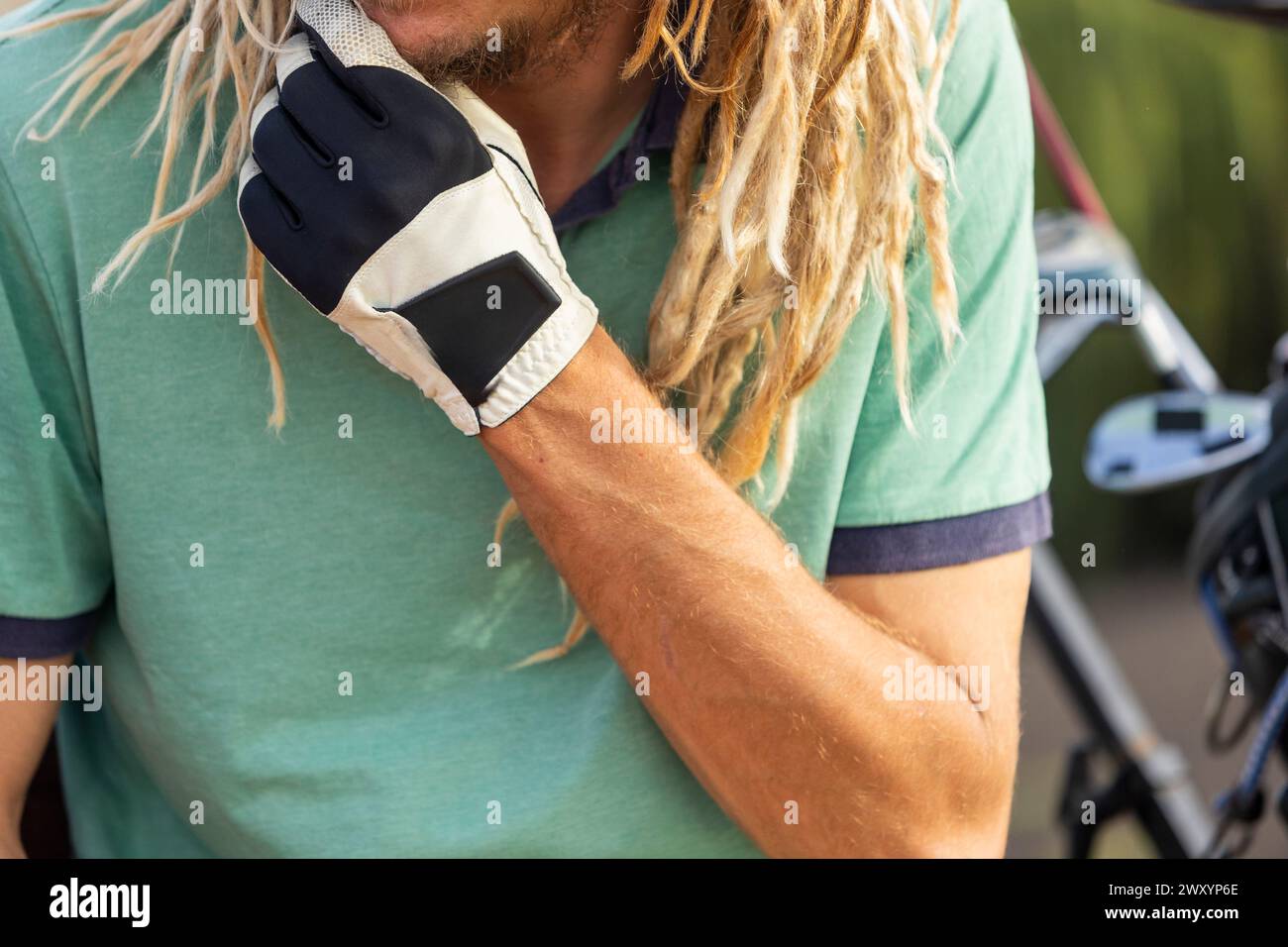 Gros plan recadré méconnaissable d'un golfeur distinctif avec des dreadlocks blonds ajustant leur gant, ajoutant un style non conventionnel à la traditiona Banque D'Images