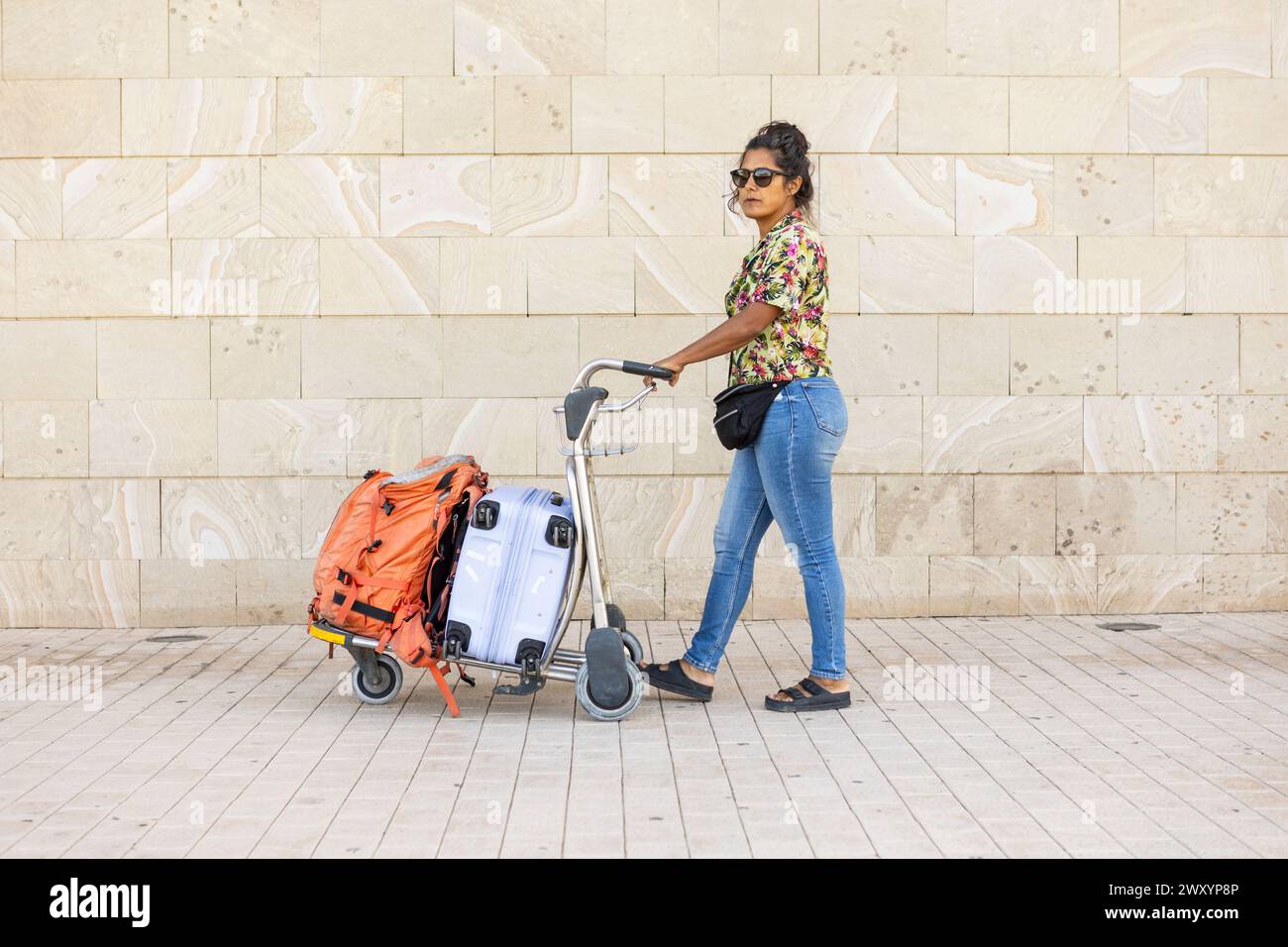 Femme à l'aéroport tirant un chariot empilé de sacs Banque D'Images