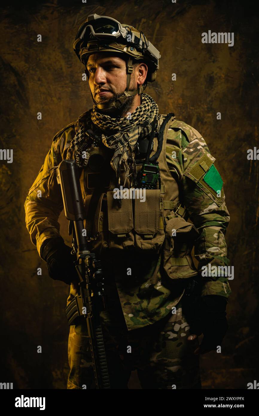 Un soldat latino-américain concentré vêtu d'équipement tactique se tient prêt, dégageant confiance et préparation dans un contexte accidenté Banque D'Images