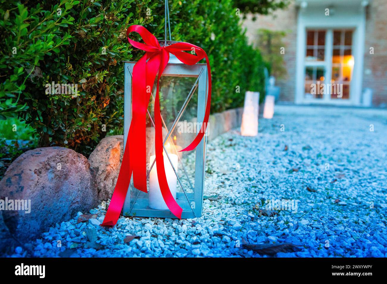 lanterne en métal avec un ruban rouge vif ajoute une touche d'élégance à un chemin de jardin au crépuscule Banque D'Images
