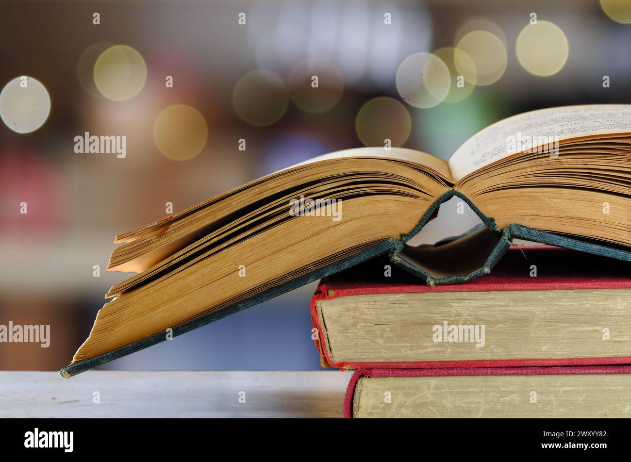 Pile de livres et livre ouvert avec fond de bibliothèque flou, lecture, apprentissage, éducation ou concept de bureau à domicile Banque D'Images