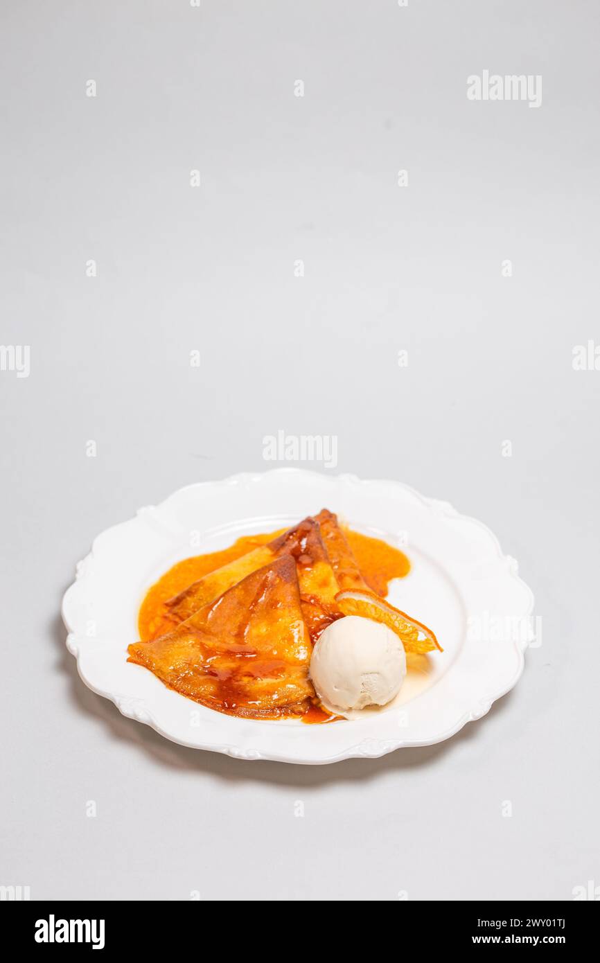 Offrez-vous un dessert alléchant de crêpes baignées d'une sauce orange et couronnées de crème glacée crémeuse pour un délice délicieux. Banque D'Images