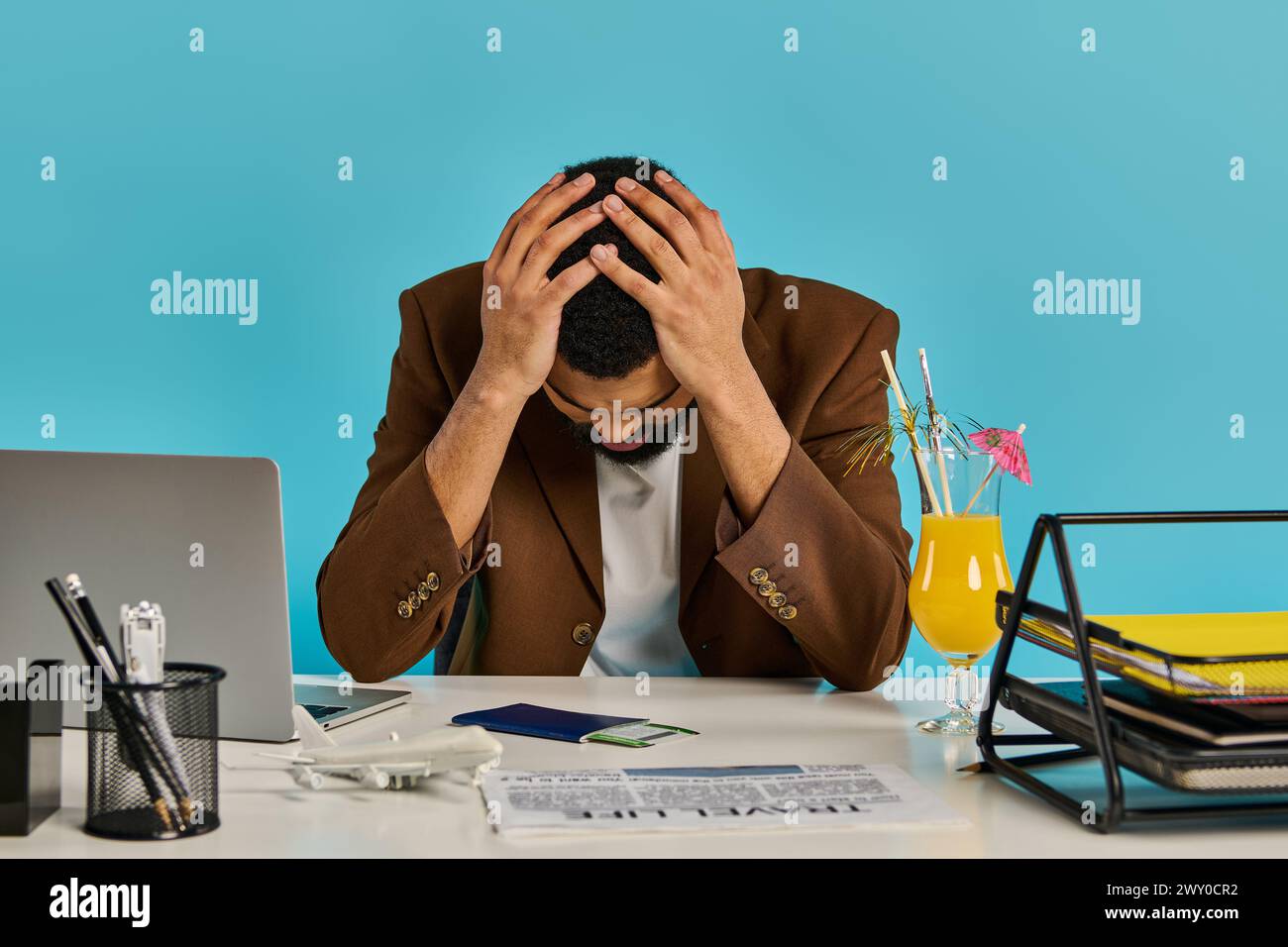 Un homme assis à un bureau, ses mains berçant sa tête dans une détresse apparente ou une pensée profonde, perdu dans l'instant. Banque D'Images