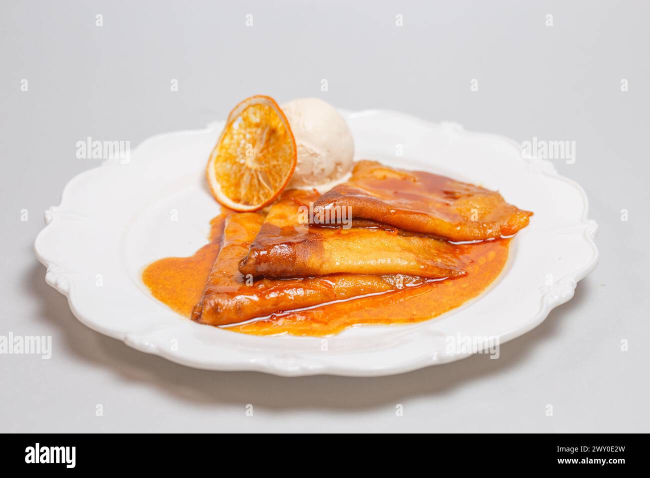 Offrez-vous un dessert alléchant de crêpes baignées d'une sauce orange et couronnées de crème glacée crémeuse pour un délice délicieux. Banque D'Images