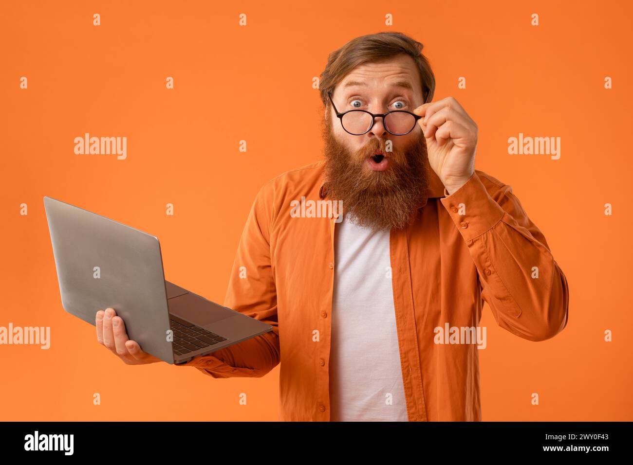 l'homme avec la barbe tient des regards d'ordinateur portable avec l'expression choquée, studio Banque D'Images