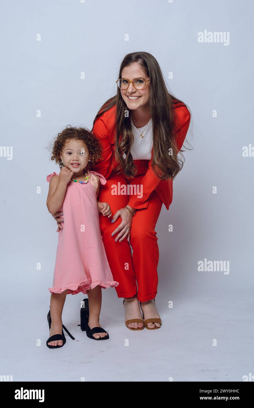 image verticale jeune femme d'affaires maman en vêtements formels rouges, debout posant avec sa fille souriant et regardant la caméra, studio shot, backgro blanc Banque D'Images