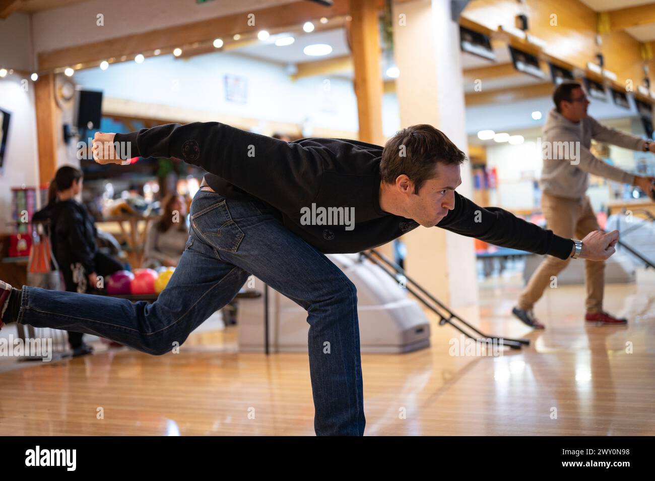 Vue latérale de la face d'effort et technique de lancer de la boule de bowling. sur un jeune joueur vêtu de noir Banque D'Images