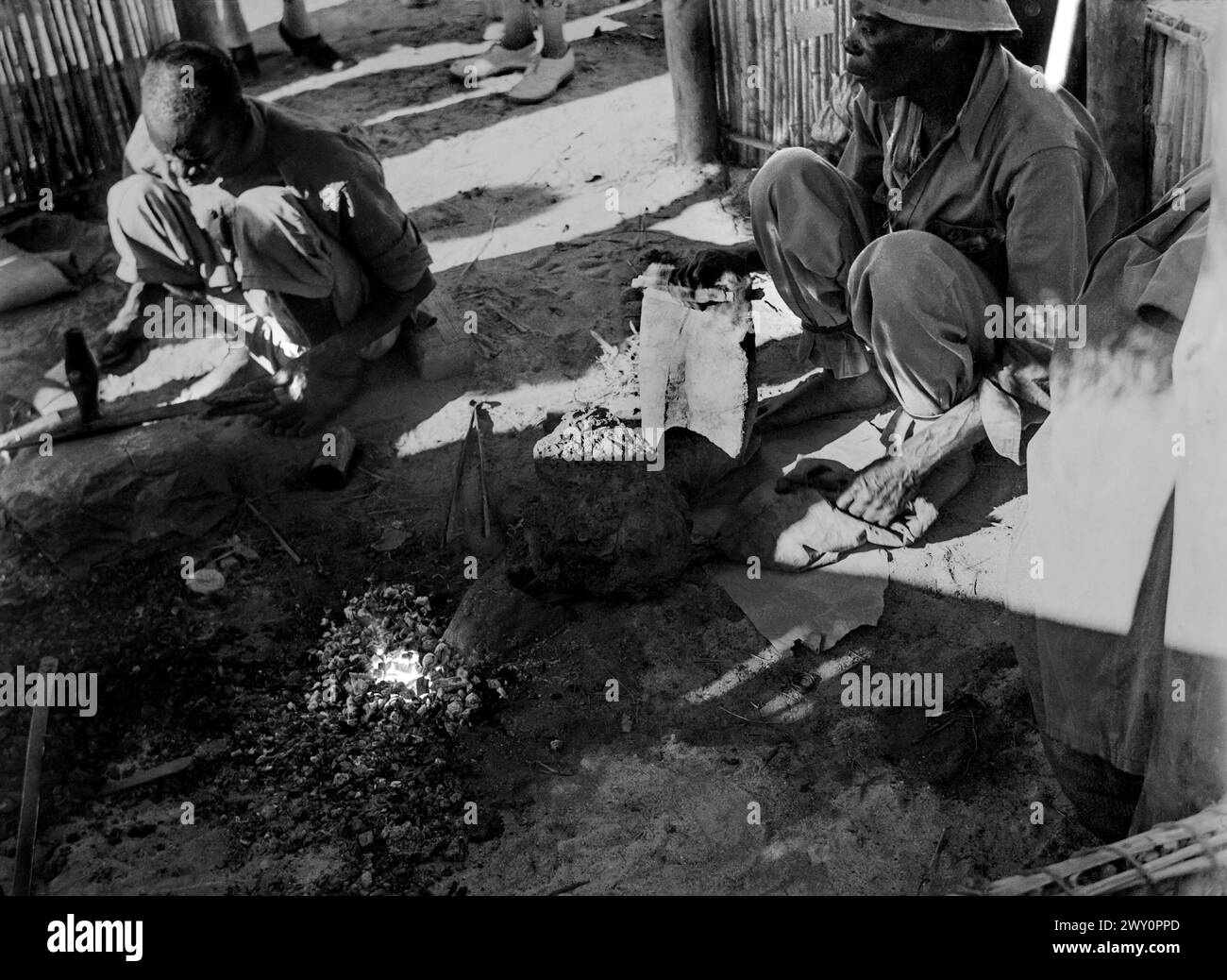 Forgerons travaillant avec un feu dans le sol alimenté par soufflet pompé à la main dans un village près de Ndola, Rhodésie du Nord (aujourd'hui Zambie) c1956 Banque D'Images