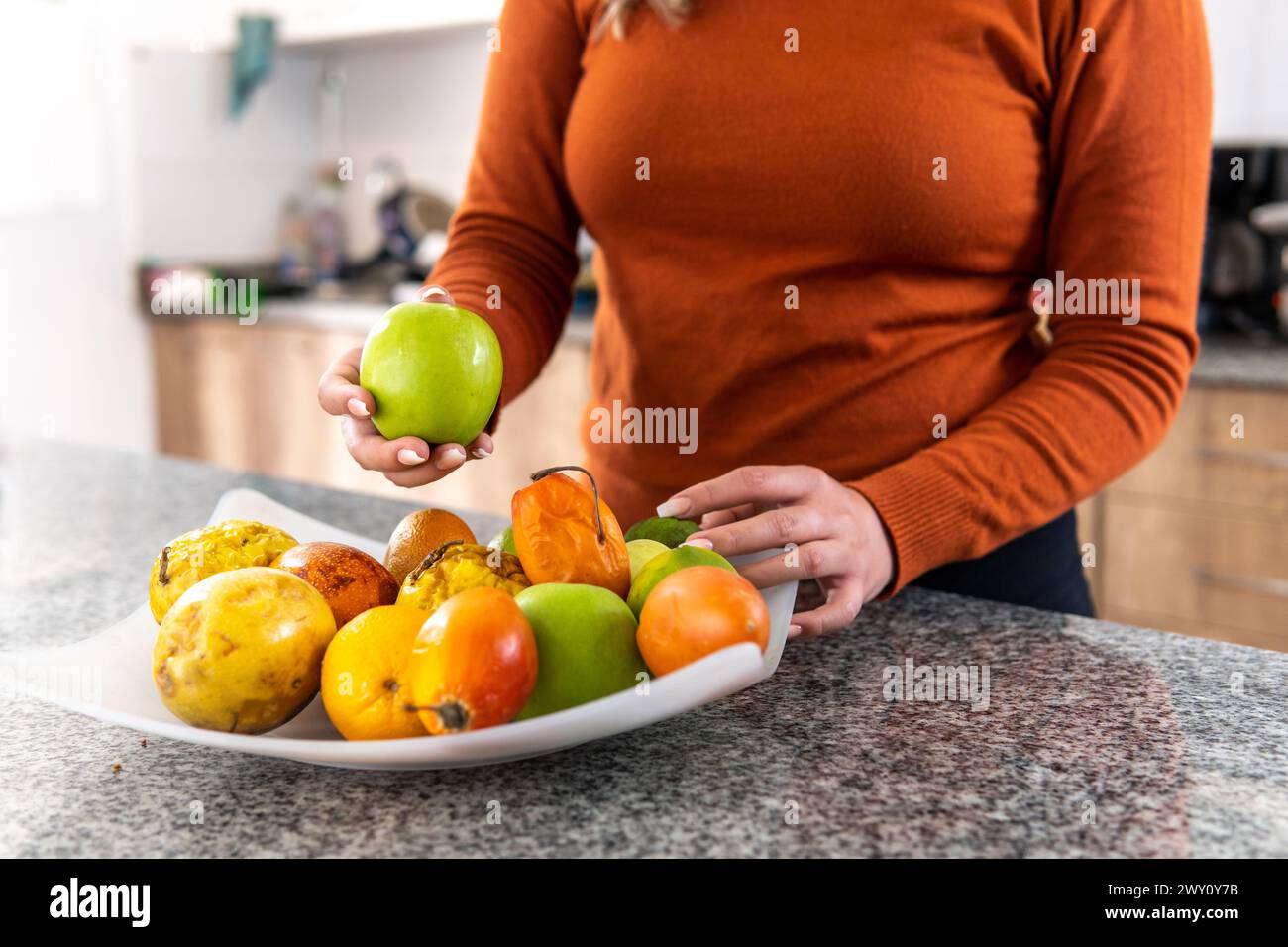 femme prenant une pomme verte d'un bol de fruits dans la cuisine le matin Banque D'Images