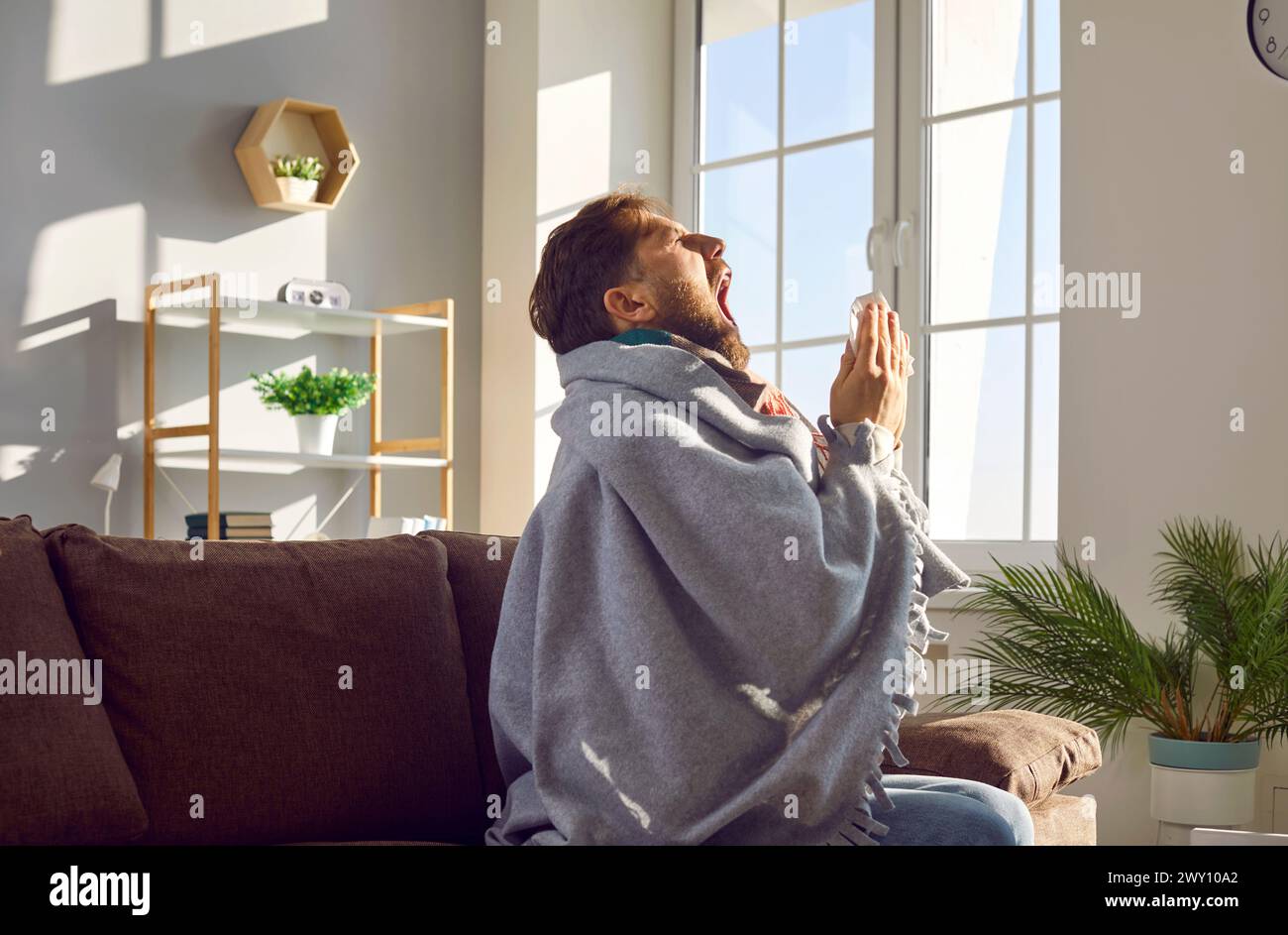 Vue latérale d'un homme malade éternuant dans une serviette à la maison. Banque D'Images