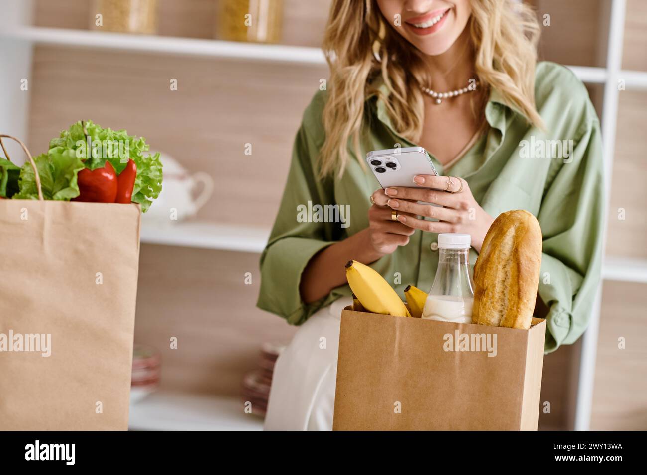 Une femme dans une cuisine regardant son téléphone portable tout en tenant un sac de nourriture. Banque D'Images