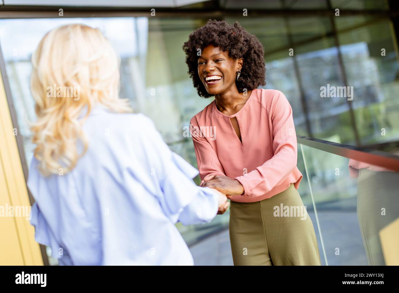 Deux femmes s'engagent dans une poignée de main amicale, l'une riant joyeusement, symbolisant une interaction positive d'affaires. Banque D'Images