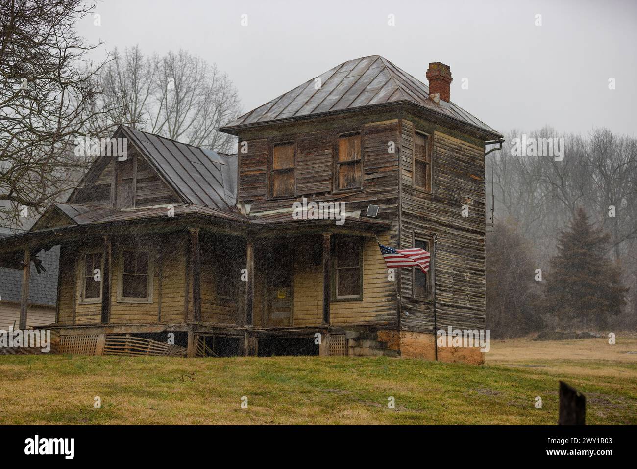 Stokesville, Virginie, États-Unis - assis négligé cette vieille maison a un drapeau américain suspendu à son porche par temps pluvieux. Banque D'Images