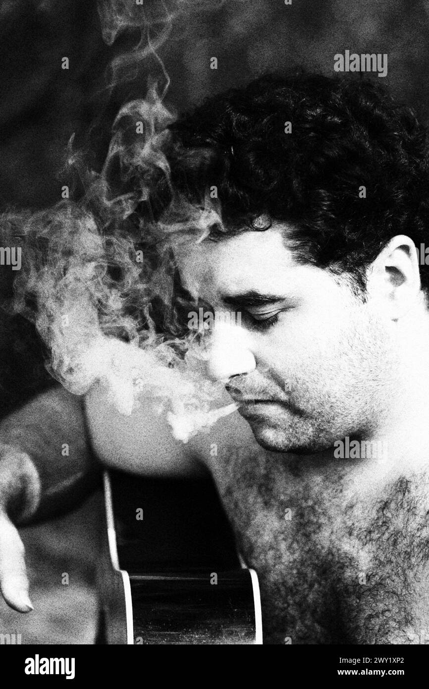 Au milieu d'une brume de fumée, un guitariste tient son instrument, les doigts posés sur des cordes, tout en se livrant à un joint, les panaches rythmiques ajoutant un surréel Banque D'Images