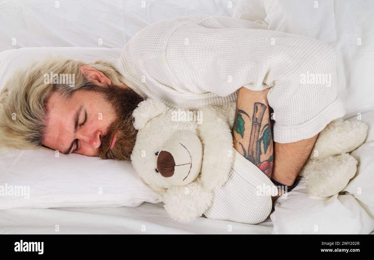 Beau homme dormant avec un ours en peluche relaxant dans le lit. Bonne nuit. Homme endormi en pyjama dormant dans le lit à la maison avec jouet ours en peluche. Barbu Banque D'Images