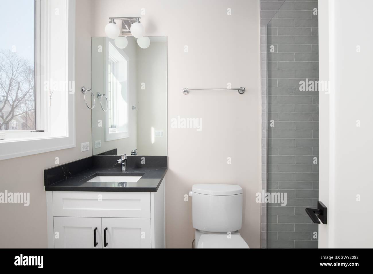 Une salle de bains avec une armoire blanche, un comptoir en marbre noir et une douche avec carrelage gris du métro. Banque D'Images