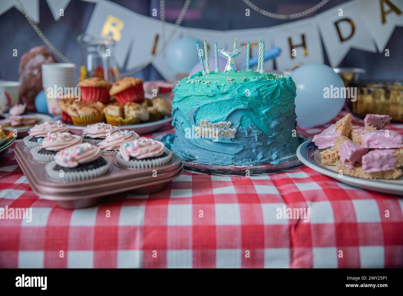 Un gâteau d'anniversaire bleu et sarcelle pour filles à thème sirène avec des bougies, des ballons, des friandises sucrées, du glaçage comestible, des muffins, cupcakes et plus encore ! Banque D'Images