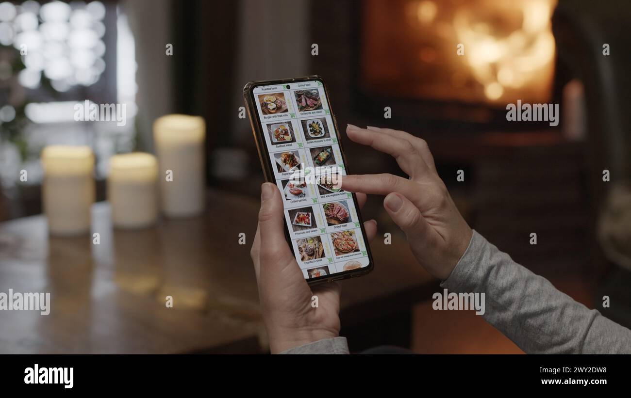 Commander de la nourriture à l'aide d'un smartphone à la maison. Une femme sélectionne la nourriture estaurant dans le menu Internet d'un restaurant gastronomique à l'aide d'une application sur un smartp Banque D'Images