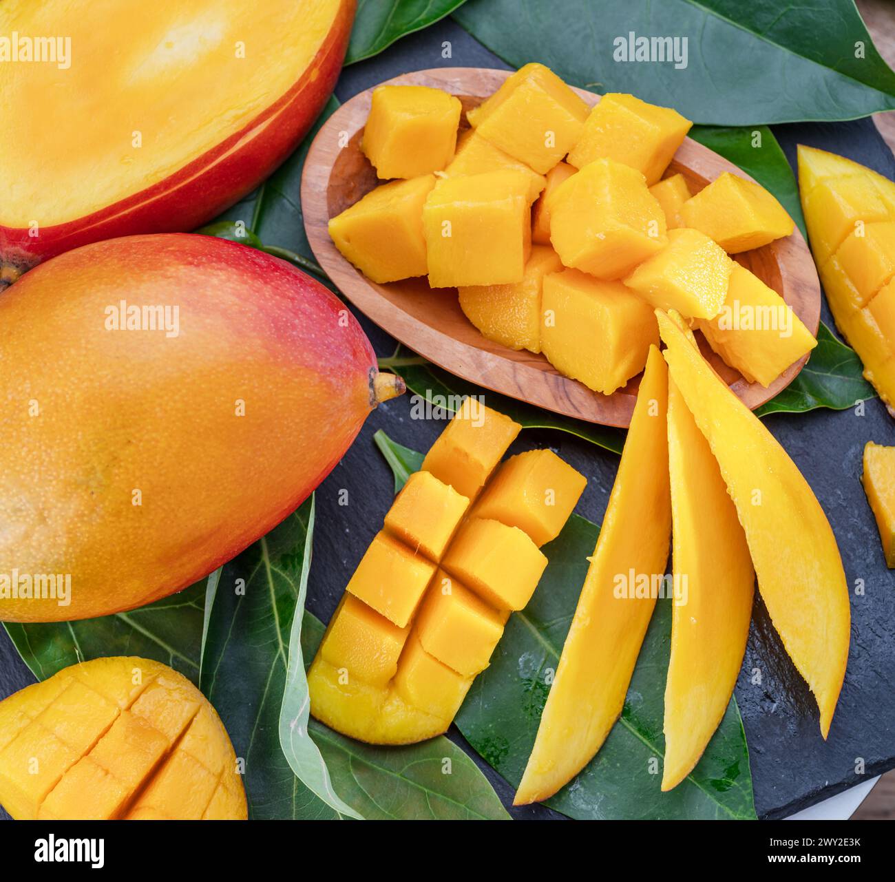 Fruits de mangue mûrs avec tranches et feuilles de mangue sur une table en pierre grise. Beau fond de fruit pour vos projets. Banque D'Images