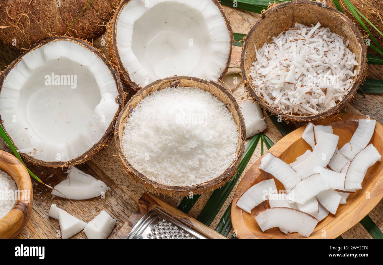 Noix de coco fraîches ouvertes avec des tranches de noix de coco, des flocons et des feuilles de noix de coco sur une table en bois. Joli fond de fruits pour vos projets. Banque D'Images