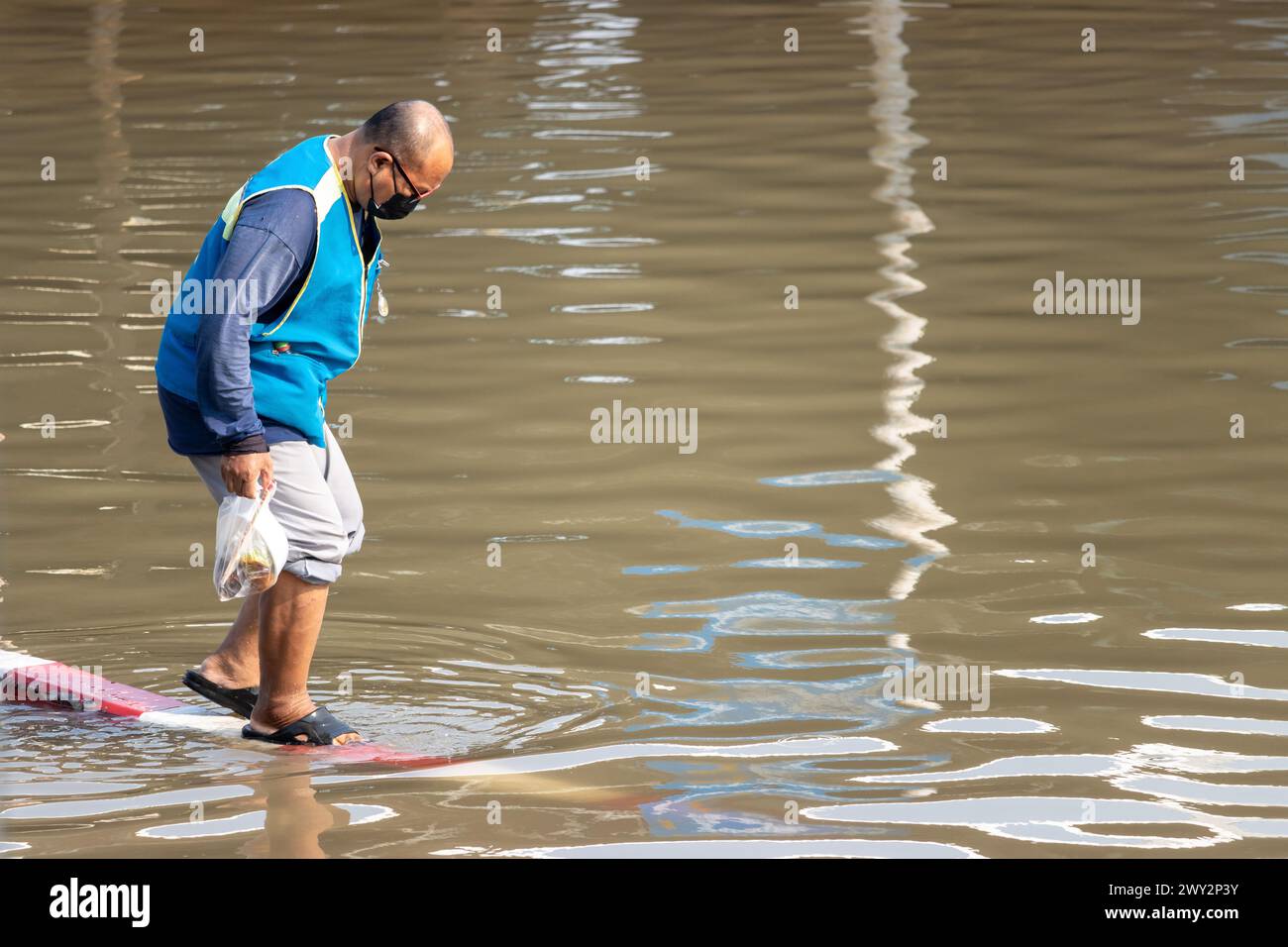 SAMUT PRAKAN, THAÏLANDE, 11 février 2024, Un chauffeur de taxi moto pénètre prudemment sur une route inondée Banque D'Images