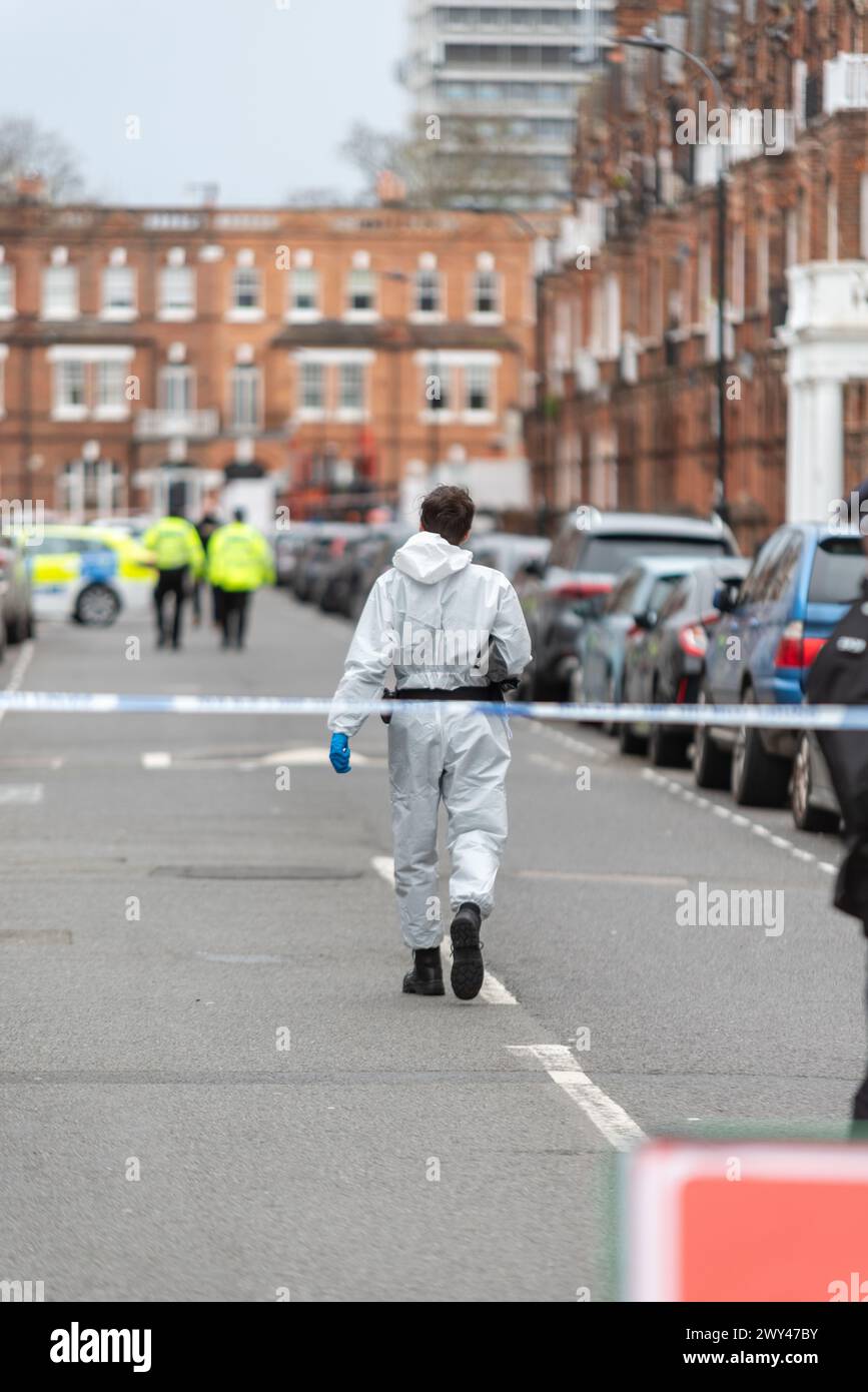 Police sur la scène d'une fusillade mortelle à Comeragh Road, West Kensington, Londres, Royaume-Uni. Officier en combinaison médico-légale se dirigeant vers la scène Banque D'Images