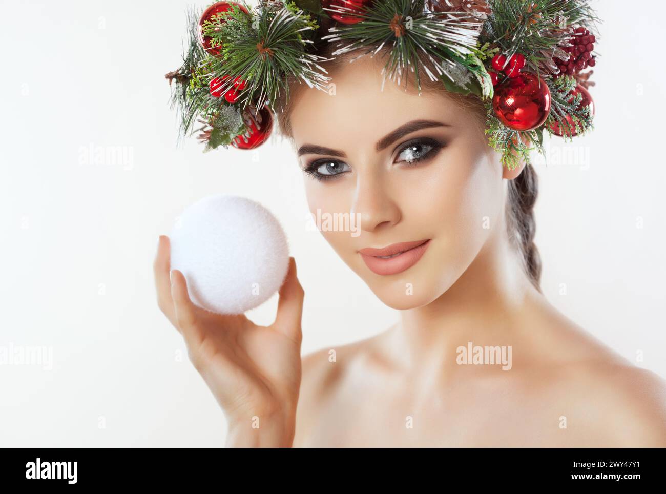 Une jolie jeune femme tient dans sa main une boule de Noël, sur sa tête une belle couronne d'épicéa avec des cônes et des boules. Concept du nouvel an. Banque D'Images