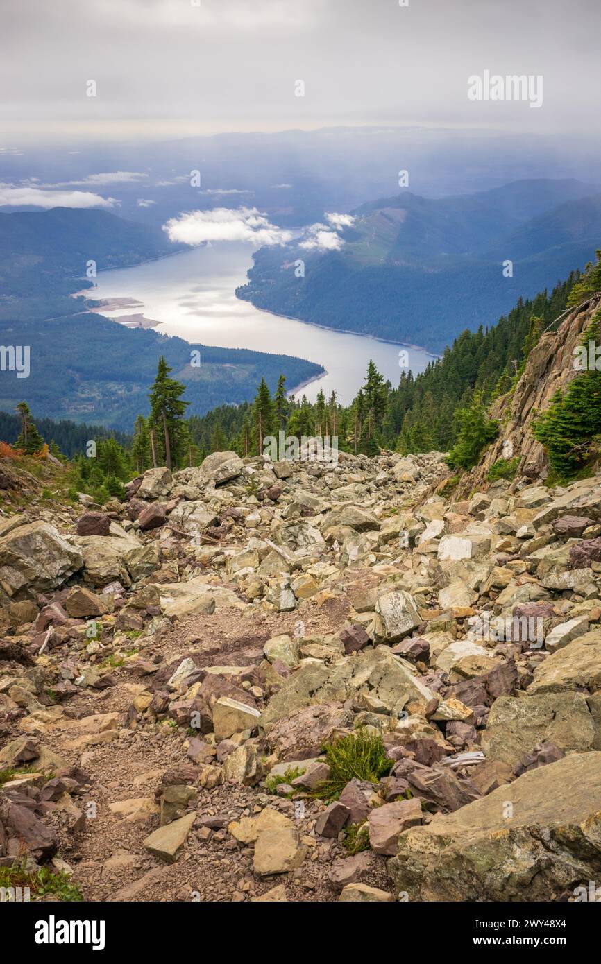 Un sentier de gravats monte un champ de débris escarpé avec le lac Cushman et les crêtes dans la brume au loin, depuis le mont Ellinor, Forêt nationale Olympique, Washington. Banque D'Images