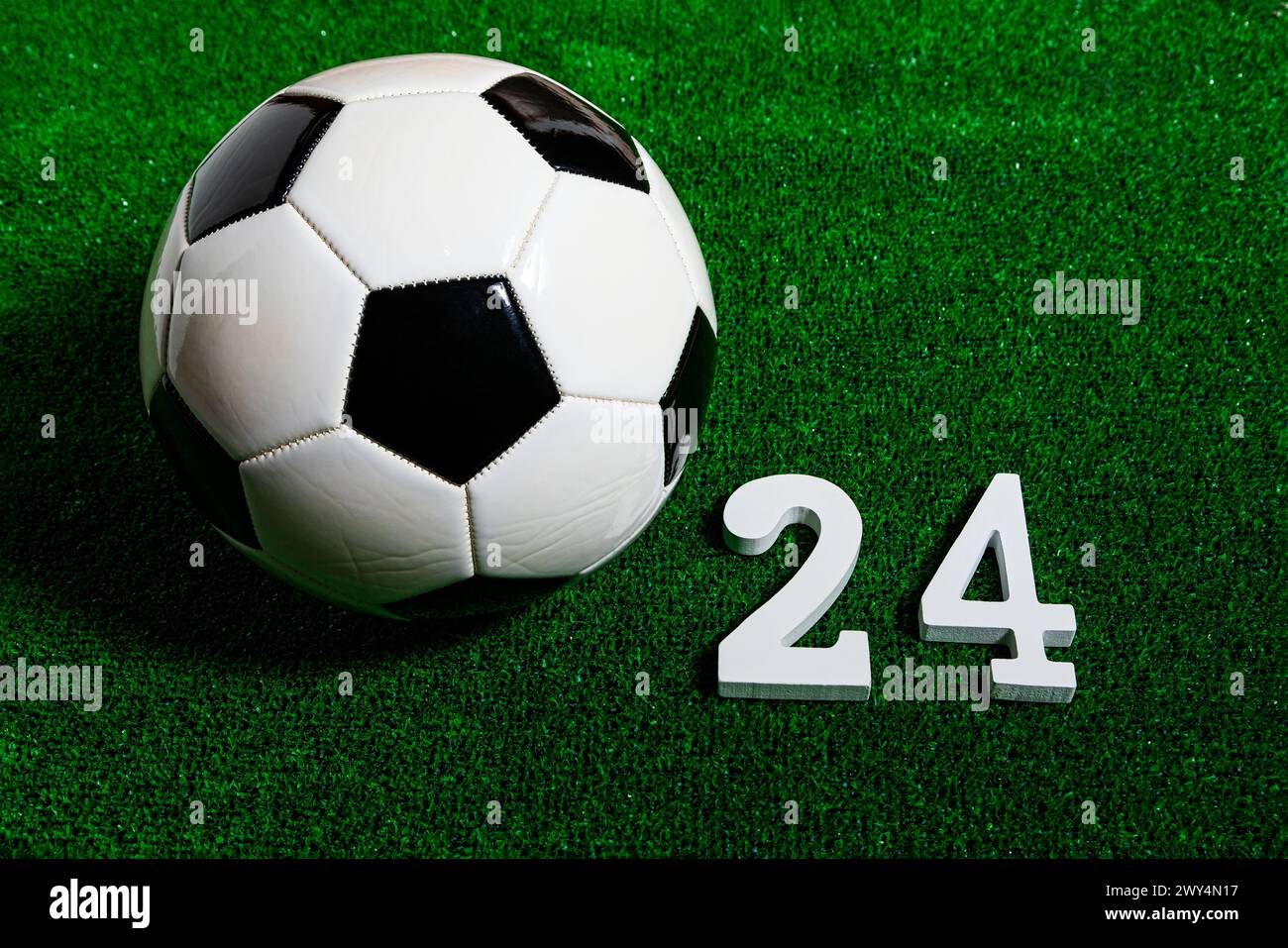 Un ballon de football noir et blanc classique sur une herbe verte déposée à côté d'un numéro en bois 24. Banque D'Images
