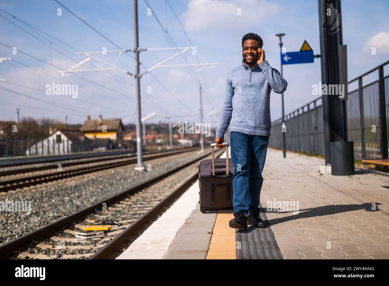 Homme heureux avec une valise parle au téléphone tout en marchant sur la gare. Banque D'Images