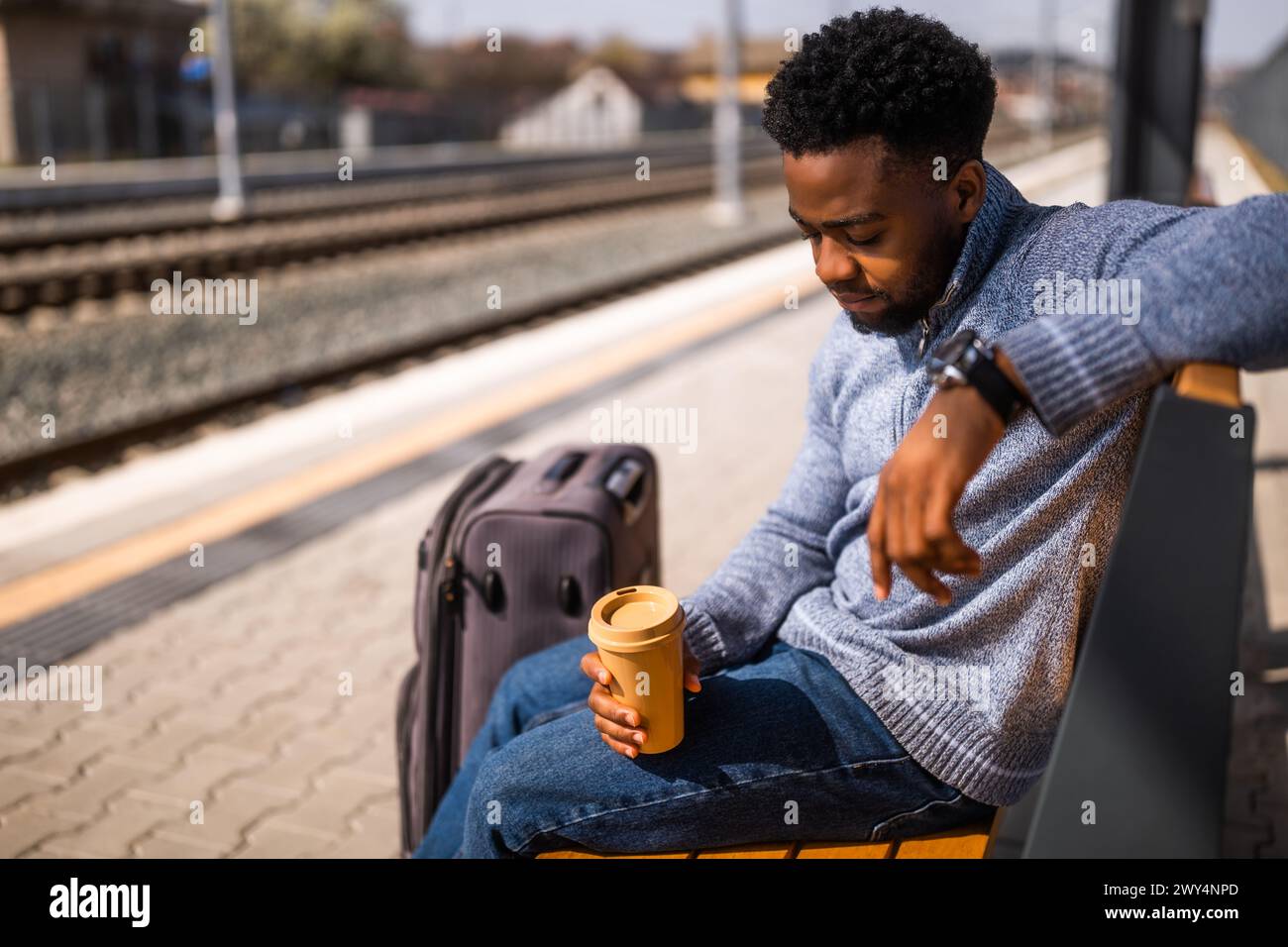 Homme fatigué avec un café dormant sur un banc à la gare. Banque D'Images